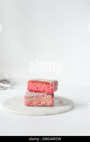 Lamingtons roses sur un plateau en marbre, lamingtons de framboises australiens, gâteau couvert de noix de coco déshydratées Banque D'Images