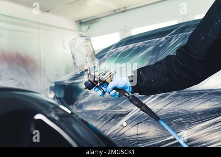 Personne portant un uniforme de protection et des gants bleus peignant une partie non couverte de la voiture à l'aide d'un aérographe. Peinture automobile. Prise de vue horizontale en intérieur. Photo de haute qualité Banque D'Images