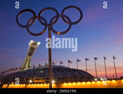 Sculpture d'anneaux olympiques en métal et stade olympique avec tour inclinée illuminée à l'aube, Montréal, Québec, Canada. Banque D'Images