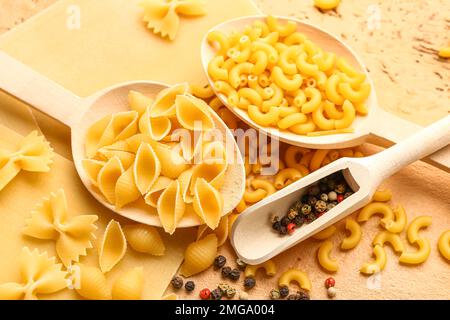 Cuillères en bois avec pâtes crues et cuillère de grains de poivre sur fond de couleur, gros plan Banque D'Images