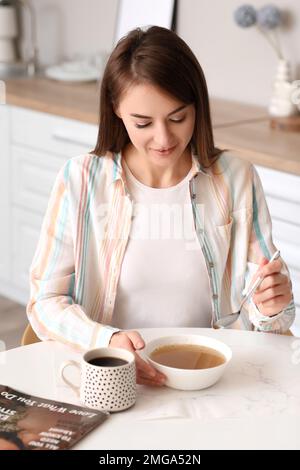 Belle femme mangeant de la soupe avec une cuillère à la table dans la cuisine Banque D'Images