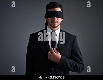 Faire des affaires dans l'obscurité. Studio photo d'un jeune homme d'affaires portant un bandeau sur fond gris. Banque D'Images