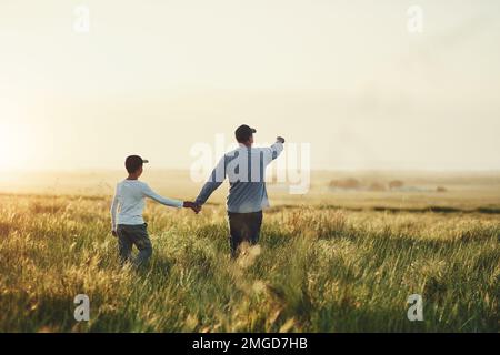 Allons explorer ce qui se passe là-bas. Vue arrière d'un père et de son fils marchant sur un champ. Banque D'Images