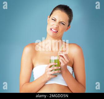 Je le regrette soudainement. Portrait studio d'une belle jeune femme qui boit une boisson verte saine et qui a l'air dégoûtée sur fond bleu. Banque D'Images