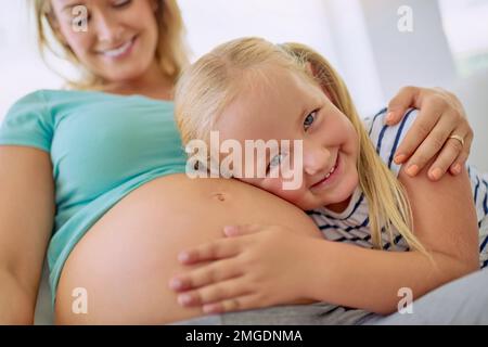 Je vais être la meilleure grande sœur et babysitter. Portrait d'une petite fille qui embrasse son ventre de mère enceinte à la maison. Banque D'Images