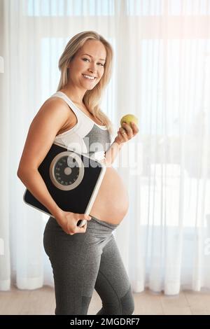 C'est le choix le plus sain pour nous deux. Portrait d'une femme enceinte heureuse vêtue de vêtements de sport et portant une balance à la maison. Banque D'Images