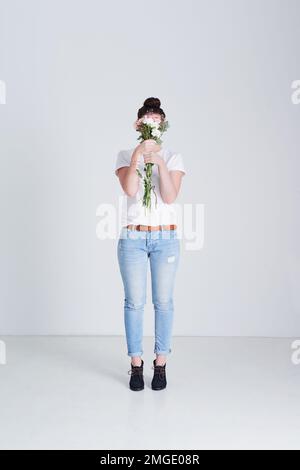 Je dois avoir des fleurs, toujours. Photo studio d'une femme méconnue couvrant son visage de fleurs sur fond gris. Banque D'Images