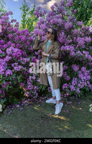 Une femme sent des fleurs pourpres sur un buisson de rhododendron, Banque D'Images