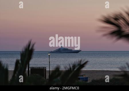 IOS, Grèce - 3 juin 2021 : vue sur un yacht de luxe à la célèbre plage de Mylopotas à iOS Grèce et un coucher de soleil violet Banque D'Images