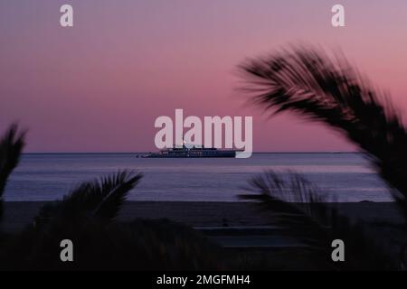 IOS, Grèce - 3 juin 2021 : vue sur un yacht de luxe à la célèbre plage de Mylopotas à iOS Grèce et un coucher de soleil violet Banque D'Images