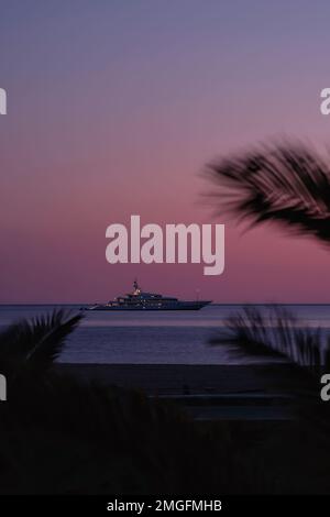 IOS, Grèce - 3 juin 2021 : vue sur un yacht de luxe à la célèbre plage de Mylopotas à iOS Grèce et un coucher de soleil violet Banque D'Images