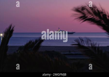 IOS, Grèce - 3 juin 2021 : vue sur un yacht de luxe à la célèbre plage de Mylopotas à iOS Grèce et un coucher de soleil violet Banque D'Images