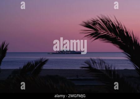 IOS, Grèce - 3 juin 2021 : vue sur un yacht de luxe à la célèbre plage de Mylopotas à iOS Grèce et un coucher de soleil violet Banque D'Images