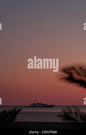 IOS, Grèce - 3 juin 2021 : vue sur un yacht de luxe à la célèbre plage de Mylopotas à iOS Grèce et un coucher de soleil violet Banque D'Images