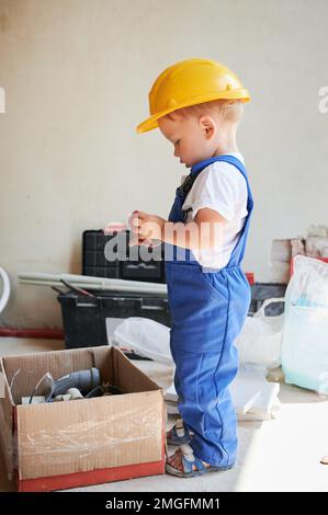 Petit garçon près d'une boîte en carton avec des outils et des matériaux pour la rénovation de la maison. Enfant ouvrier de construction tenant un composant de construction. Banque D'Images