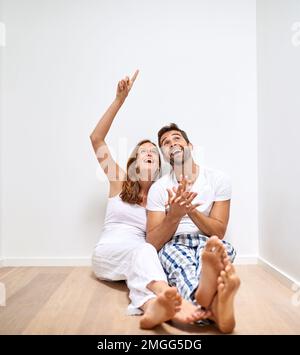 Nous devrions absolument y mettre un puits de lumière. un jeune couple heureux assis sur le sol et en admirant leur nouvelle maison. Banque D'Images