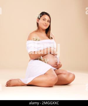 Grossesse, beauté et portrait d'une femme en studio avec du matériel de mousseline et des fleurs tenant son estomac. Maternité, santé prénatale et grossesse Banque D'Images