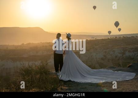 Cappadoce, Turquie-20 septembre 2022: Beau couple élégant dans l'amour se tient contre le fond des ballons à l'aube et tient les mains. Banque D'Images