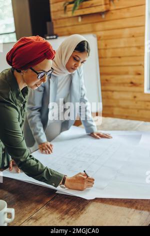 Deux concepteurs musulmans travaillant sur des plans-plans dans un bureau moderne. Des femmes d'affaires innovantes planifiant un nouveau projet créatif. Deux femmes architectes Banque D'Images