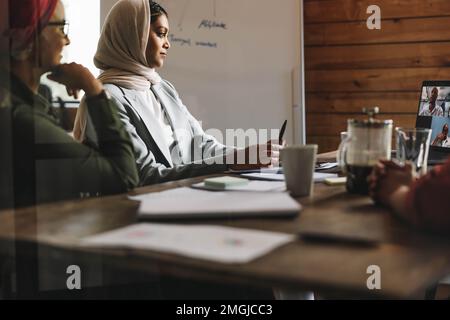 Femmes entrepreneurs assistant à une réunion en ligne dans un bureau moderne. Femmes d'affaires musulmanes ayant une vidéoconférence avec leurs associés d'affaires moi Banque D'Images