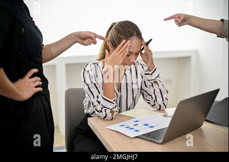 Une jeune employée de bureau asiatique stressée et déprimée s'assoit à son bureau et reçoit une plainte de son patron, en étant pointue du doigt de son responsable. obtenir Banque D'Images