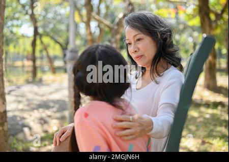 Une grand-mère asiatique heureuse et gentille racontant une histoire à sa petite-fille tout en se relaxant dans le parc ensemble. concept « happy family time » Banque D'Images