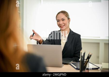 Une femme asiatique heureuse et amicale du millénaire qui a interviewé un candidat à un poste, en parlant avec un nouvel employé dans le bureau. Banque D'Images