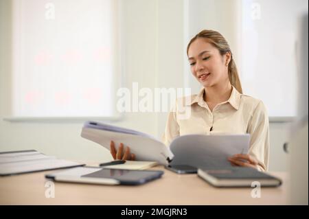 Femme d'affaires ou comptable asiatique du millénaire attirante et professionnelle examinant un rapport d'affaires à son bureau. Banque D'Images