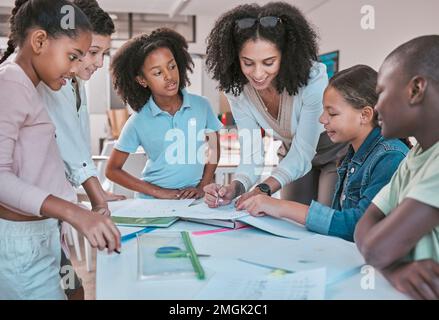 Enseignante en classe avec les élèves, aidant l'apprenant à faire ses devoirs et à écrire dans le livre. Éducation des enfants à l'école, éducateur lisant les enfants Banque D'Images