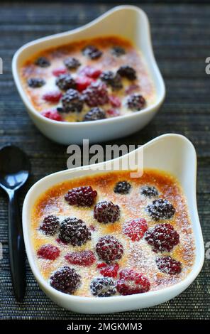 Gratin de fruits avec baies, framboises, mûres et crème dans des plats blancs sur la table pour le dessert Banque D'Images