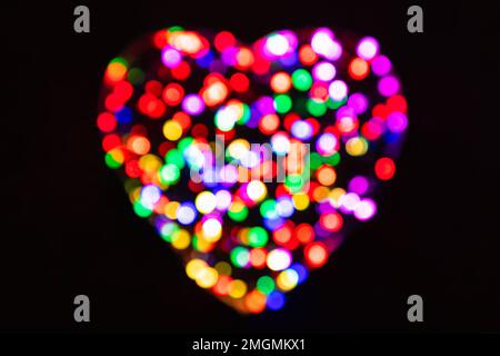 Cercles confetti défocurés arc-en-ciel de la lumière en forme de coeur sur fond noir avec effet bokeh Banque D'Images