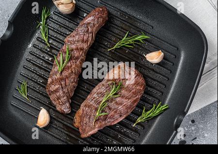 Rôti sur une poêle à frire à rabat ou sur une viande de bœuf Bavette au romarin. Arrière-plan gris. Vue de dessus Banque D'Images