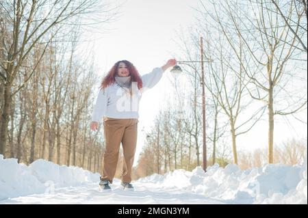 Femme souriante à tête rouge et relief sautant dans le parc en hiver. Banque D'Images