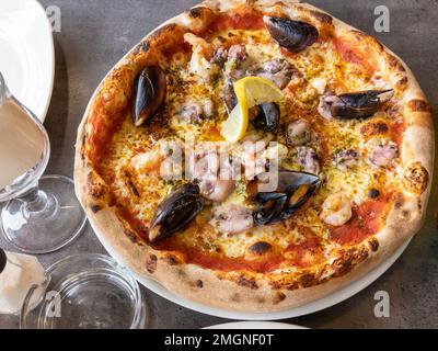 Pizza de fruits de mer avec moules crevettes calmars et une tranche de citron dans une assiette blanche dans le restaurant sauce tomate rouge fromage sur fond de table rustique ITA Banque D'Images