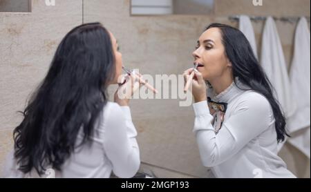 Une jeune femme fait quotidiennement soin du visage avant d'aller au travail, peint ses lèvres avec du rouge à lèvres. Brunette dans la salle de bains se préparer pour le travail. Banque D'Images