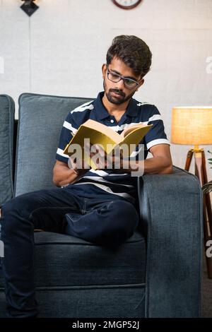 Plan vertical du livre de lecture de jeunes indiens sérieux pendant le temps libre à la maison - concept d'éducation, passe-temps et travailleur dur. Banque D'Images