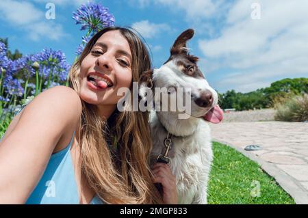 Portrait selfie de la jeune femme colombienne Latina, avec son chien collie frontière, dans le parc en collant sa langue et regardant l'appareil photo, avec les s. Banque D'Images