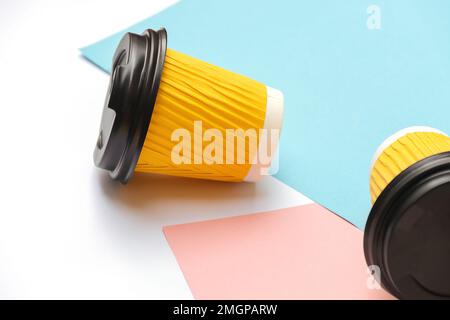 Deux tasses jaunes de café à emporter se trouvent dans un désordre créatif sur du papier coloré sur une table de design. Fond bleu, orange et rose. Copier l'espace pour le texte Banque D'Images