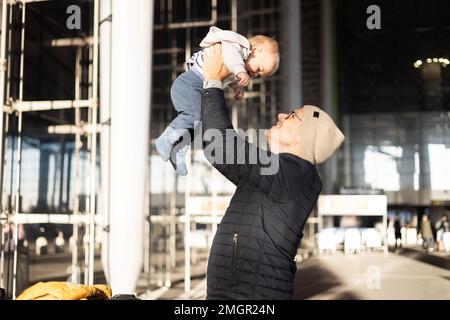 Le père se fait un plaisir de tenir et de soulever son bébé garçon enfant dans les airs après avoir été réjunté devant la gare de l'aéroport. Concept de voyage pour bébé Banque D'Images