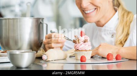 Les femmes professionnelles de pâtisserie comme pâtisserie ont drapé des morceaux de chocolat sur un muffin garniture avec brucelles Banque D'Images