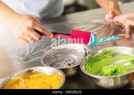 les femmes de pâtisserie comme pâtisserie préparent différentes couleurs de crème pour le sac de glaçage pour piquage de la garniture de muffin Banque D'Images