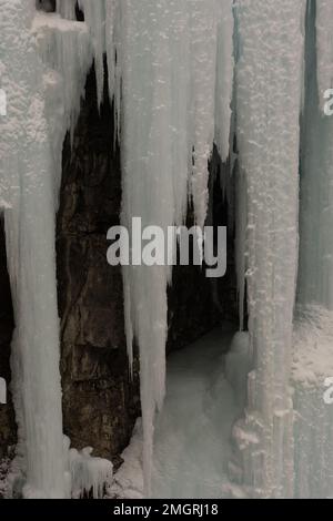Un cliché vertical de glaçons aux bords tranchants accrochés au mur en hiver à la lumière du jour Banque D'Images