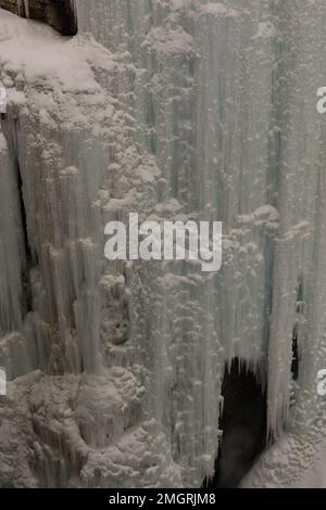 Un cliché vertical de glaçons aux bords tranchants accrochés au mur en hiver à la lumière du jour Banque D'Images