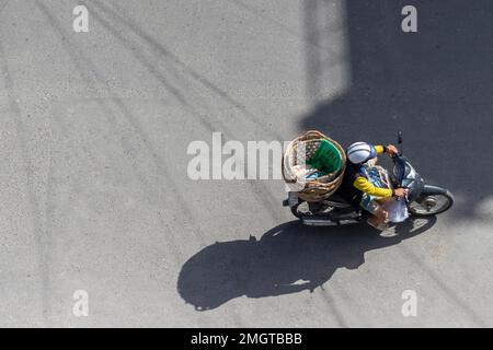 Nha Trang, Vietnam - 7 janvier 2019: Une femme conduit une moto avec des paniers vides sur l'asphalte. Vue de dessus. Banque D'Images