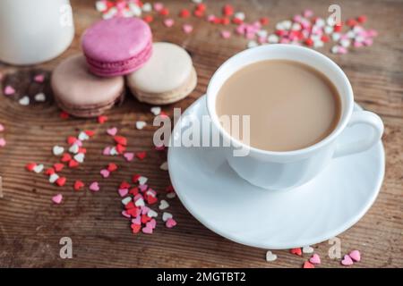 Macarons et une tasse de café, un pot à lait sur un fond de petits coeurs sur un fond de bois, vue du dessus Banque D'Images