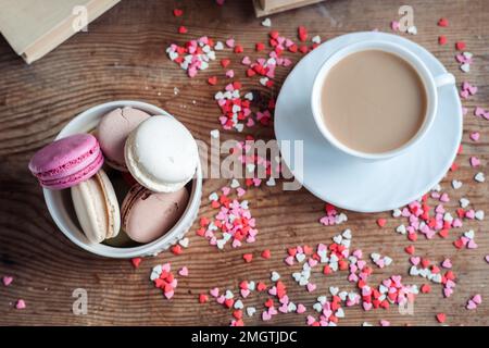 Macarons dans un bol et une tasse de café, sur fond de petits coeurs sur fond de bois, vue de dessus Banque D'Images