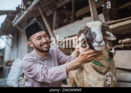 un homme musulman qui s'accroupite à côté de la chèvre et qui lui fait un tour de cou Banque D'Images