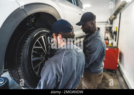 Mécaniciens de voitures remplaçant les roues d'une automobile soulevée dans un poste de réparation. Photo de haute qualité Banque D'Images