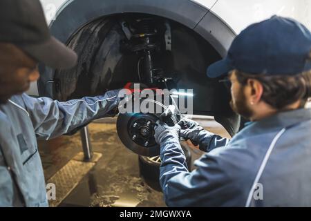 Mécanicien remplaçant les roues d'une voiture de luxe blanche à l'aide d'outils dans un atelier de réparation automobile. Photo de haute qualité Banque D'Images