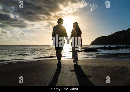 silhouette de jeune couple engagé tenant les mains amoureuses pendant le coucher du soleil sur une plage de sable Banque D'Images